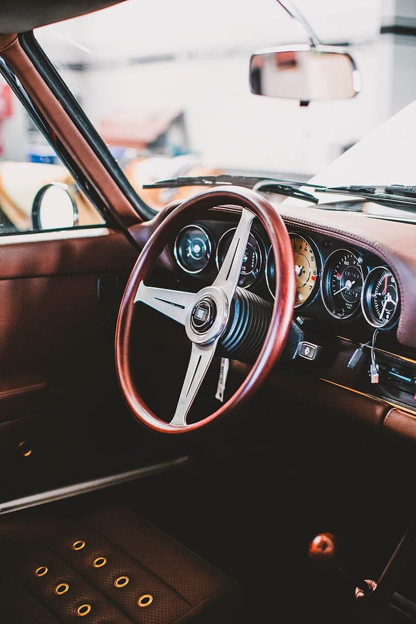 Polished mahogany steering wheel and stitched leather dashboard featuring analog gauges in a classic car interior.