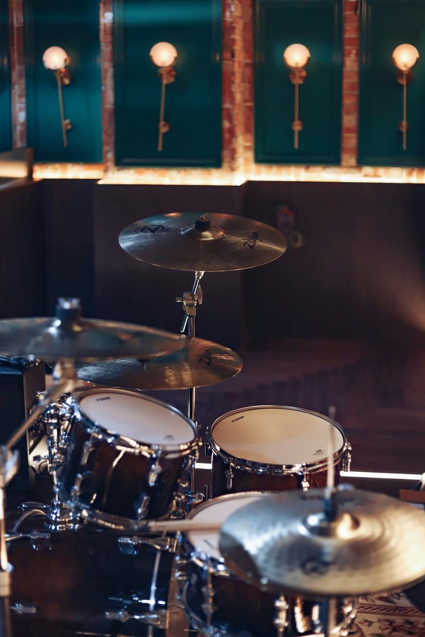 Mahogany drum set with golden cymbals illuminated by minimalist glowing wall sconces in a dark studio.