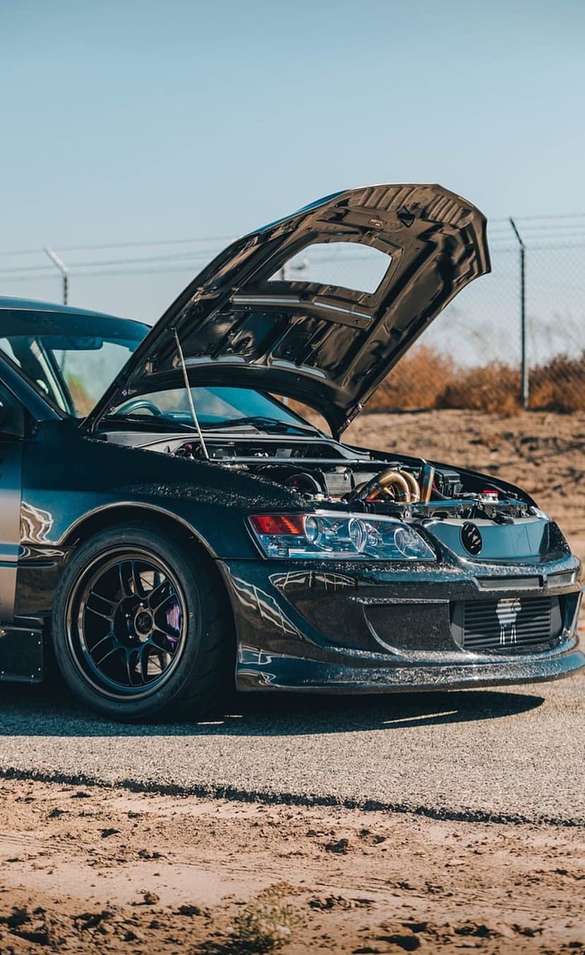 Black Mitsubishi Lancer Evolution with an open hood showcasing a modified engine bay under a clear blue sky.