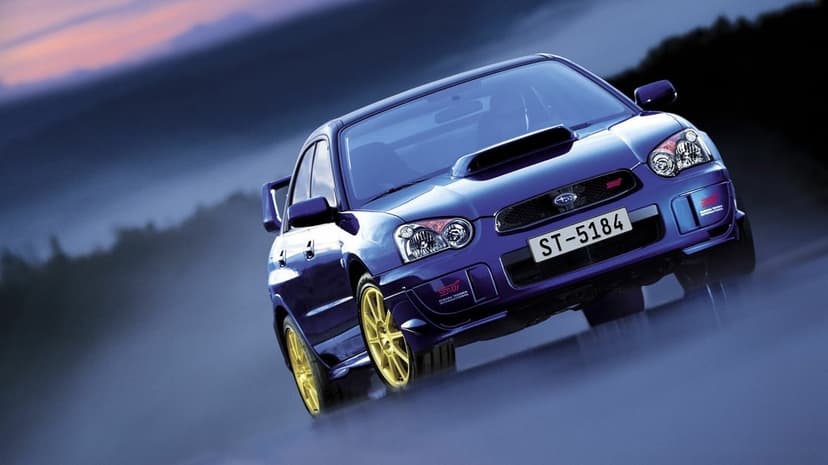 Blue Subaru Impreza WRX STi with gold wheels and hood scoop parked on a misty, blurred background.
