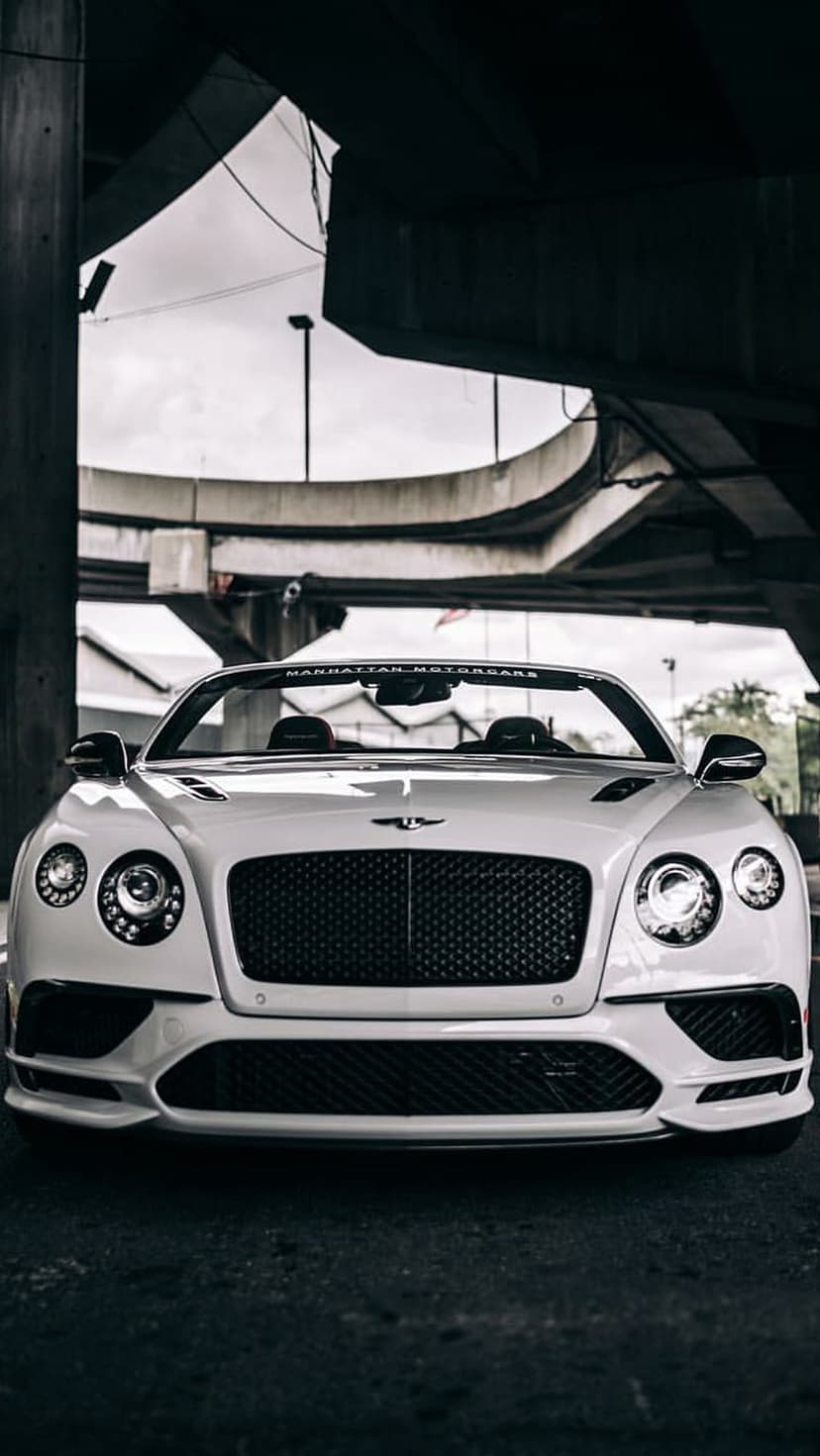 White Bentley convertible with a classic grille parked under a concrete bridge with dramatic urban shadow lighting.