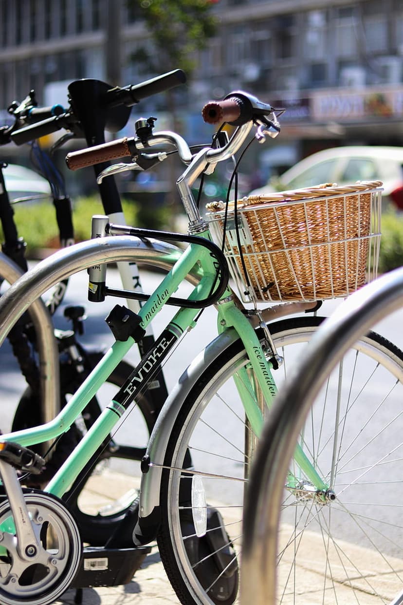 Mint green Evoke bicycle with a woven wicker basket on silver handlebars and black fenders in a close-up view.