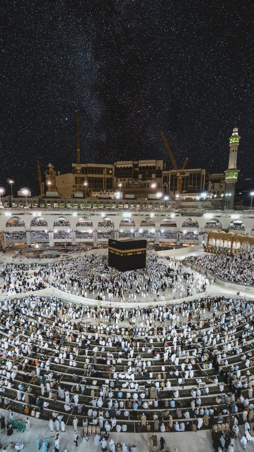 The Kaaba sits centered in the Masjid al-Haram courtyard under a dense field of stars during a clear night.