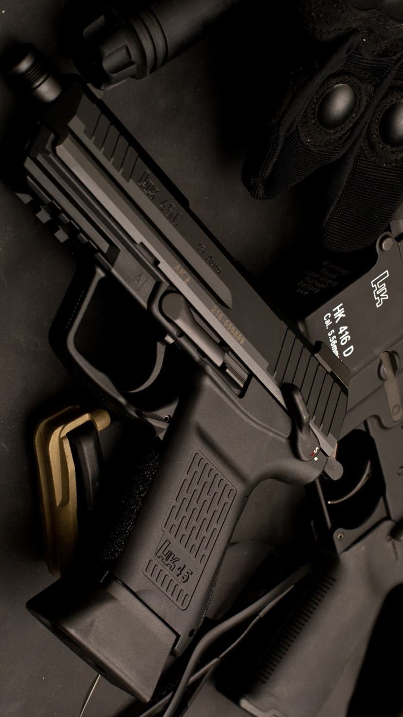 Black HK USP 45 pistol and detached magazine lie near tactical gloves under moody, low-key lighting.