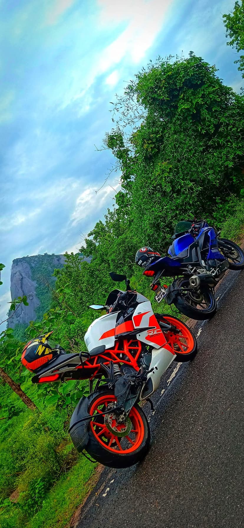 White, orange, and blue sport motorcycles parked on an asphalt road with a massive rocky mountain in the distance.