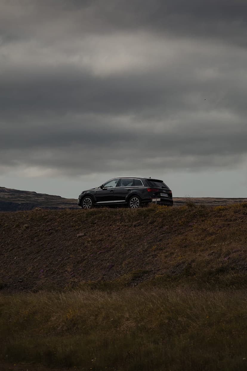 Dark SUV parked on a brown grassy hill beneath a heavy overcast sky during a moody, dim and atmospheric afternoon.