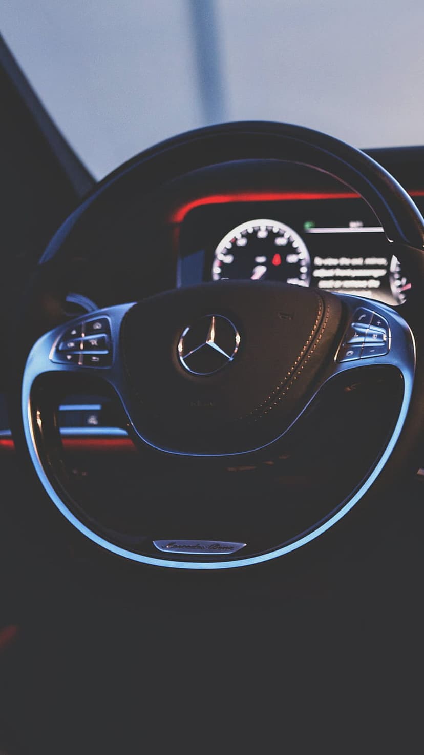 Mercedes-Benz steering wheel with chrome star logo centered against a glowing red digital dashboard display.
