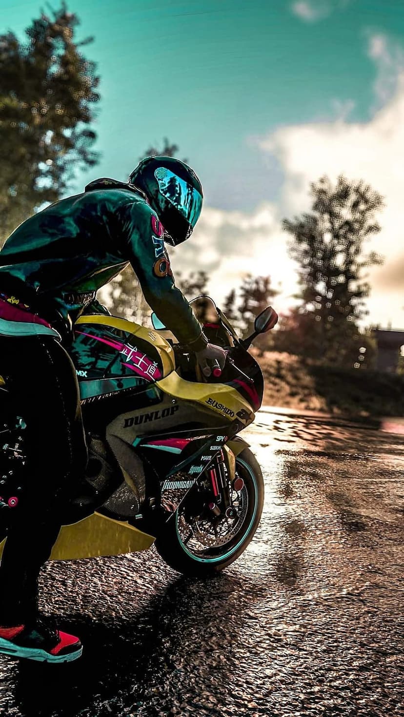Motorcyclist in green racing gear sits on a yellow bike on a wet road with a blue visor and long shadows.