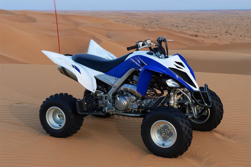 Blue and white sport quad parked on vast orange sand dunes under a clear desert sky in soft daylight.