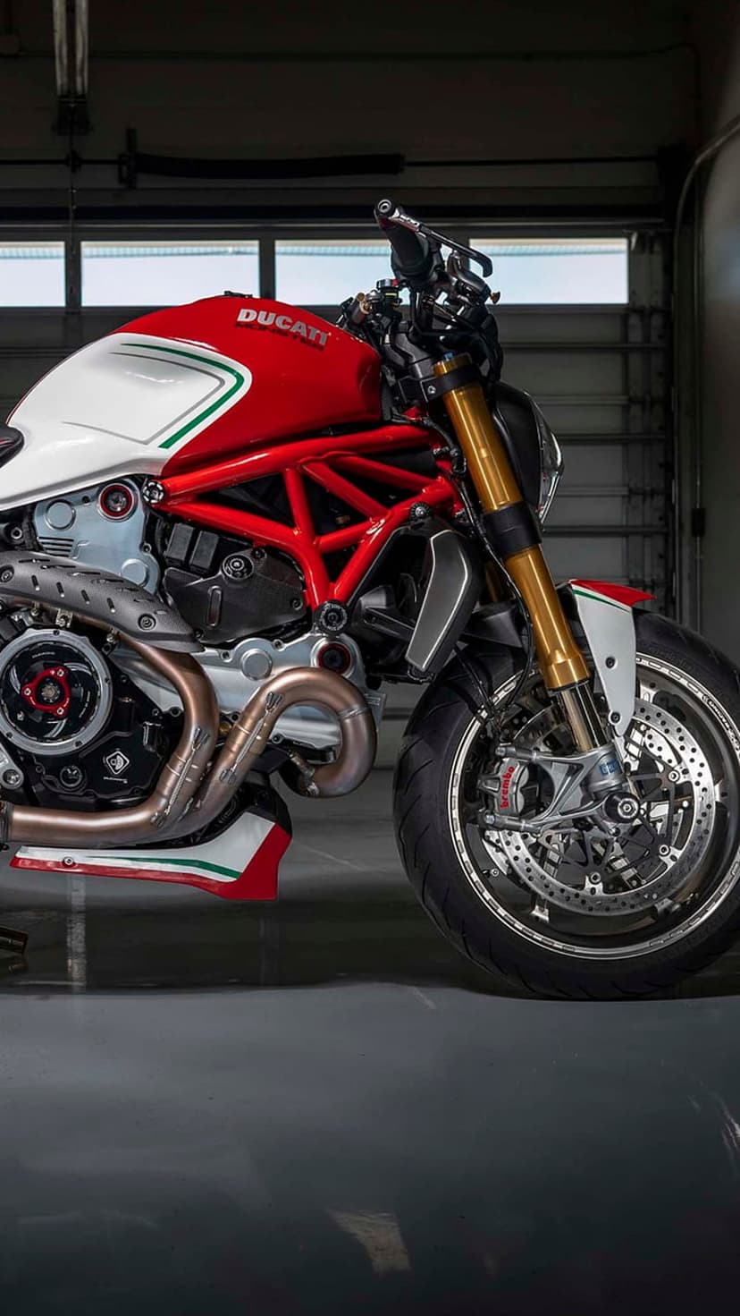 Red and white Ducati motorcycle with gold forks and a trellis frame stands on a reflective garage floor.