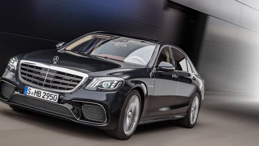 Black Mercedes-Benz S65 AMG luxury sedan driving fast past a dark metallic wall with visible motion blur.