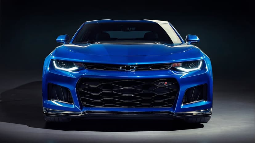 Front view of a blue Chevrolet Camaro ZL1 with glowing LED headlights and a black honeycomb grille in a dark studio.