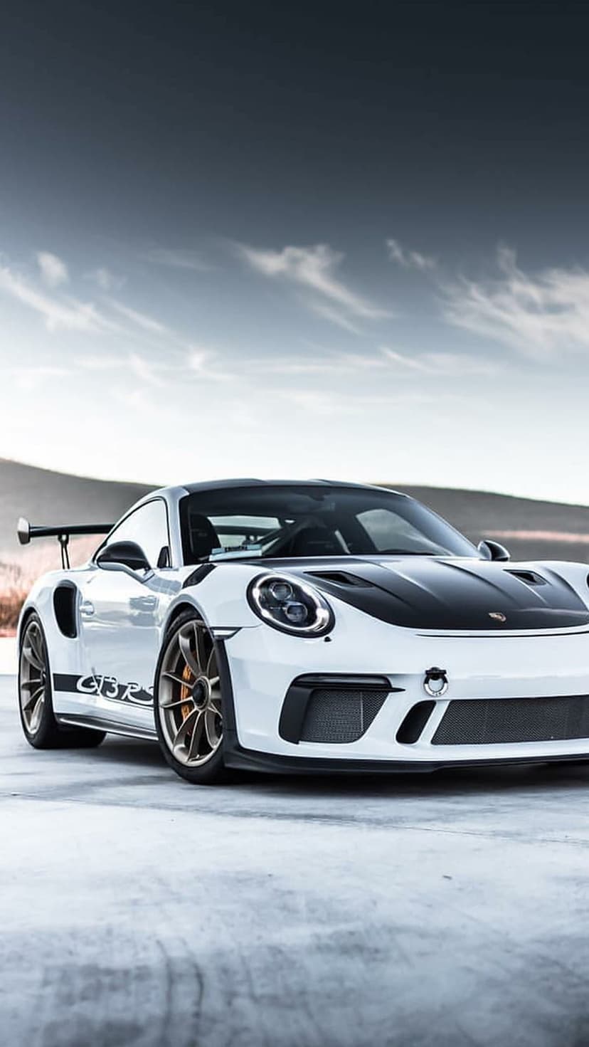 White Porsche 911 GT3 RS with black hood and rear wing on a concrete road with hazy mountains in the background.