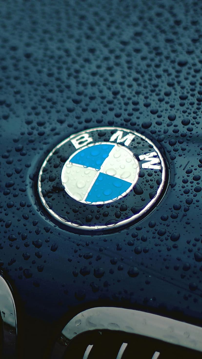 BMW emblem on a black car hood covered in small water droplets with a sharp focus on the silver metallic edges.