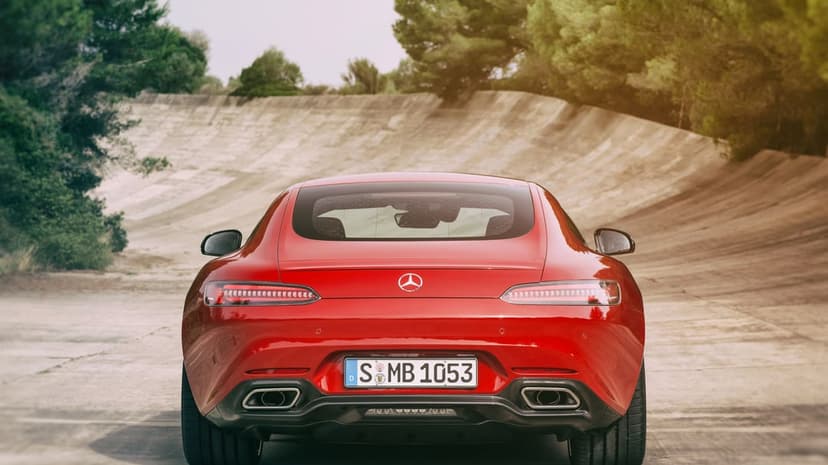Rear view of a red Mercedes-AMG GT on a curved concrete race track with trees under warm sunlight.