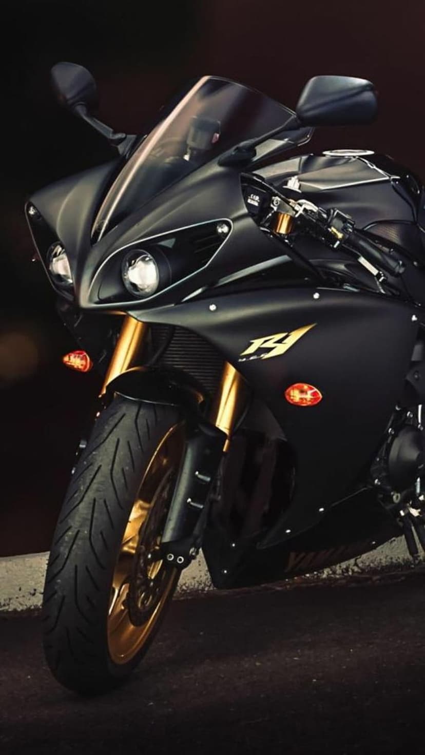 Yamaha R1 motorcycle in matte black with gold front forks and wheels against a dark atmospheric background.