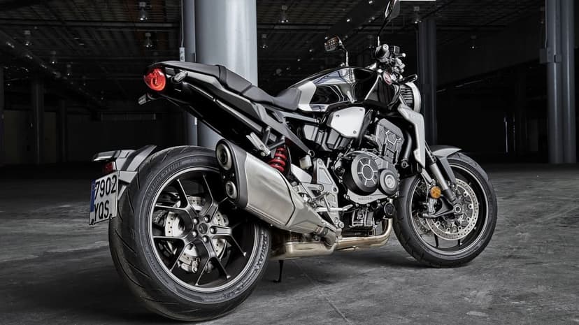 Honda CB1000R motorcycle in a dark industrial garage with silver exhaust and black bodywork.