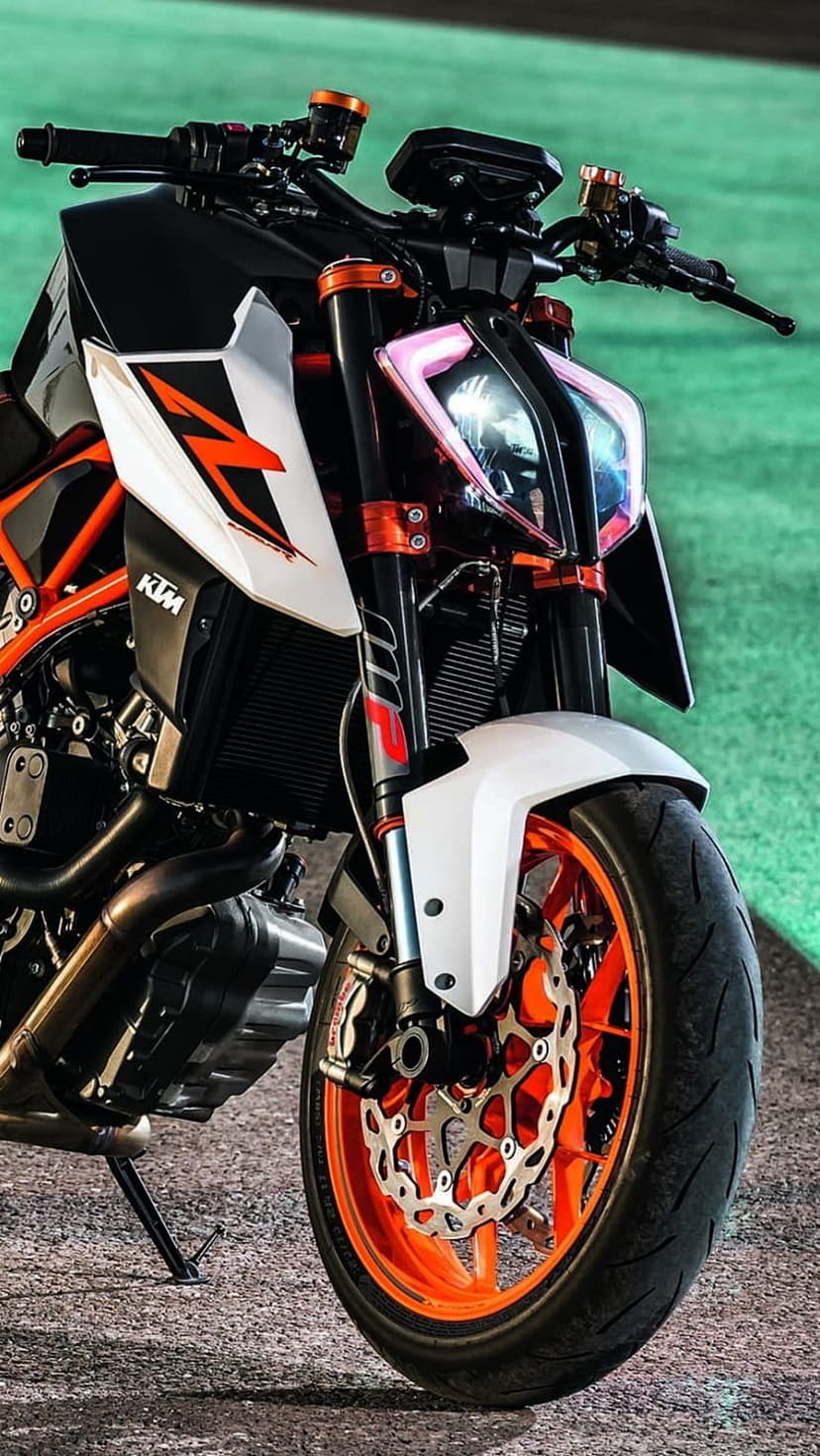 KTM motorcycle front wheel with an orange rim, LED headlight with pink glow, and silver suspension forks.