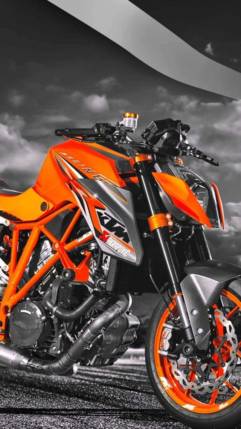 KTM superbike with an orange frame and Akrapovic exhaust sits against a dramatic grayscale sky with sharp lighting.