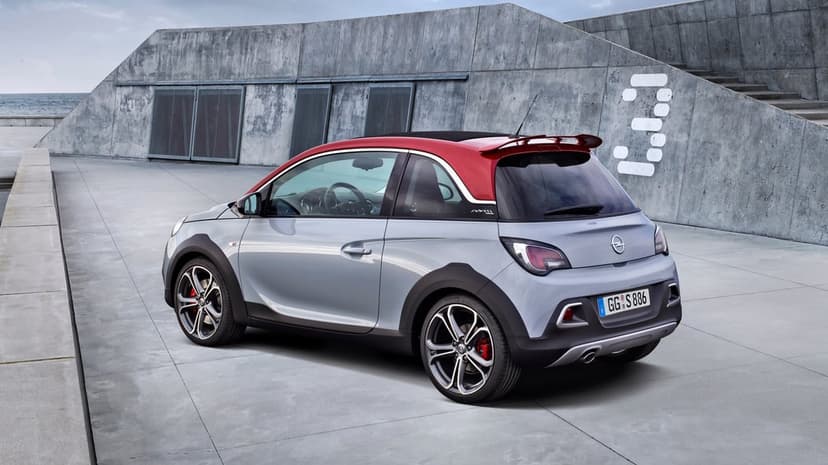 Silver Opel Adam with a red roof and spoiler parked on a grey concrete ramp against a modern concrete wall.