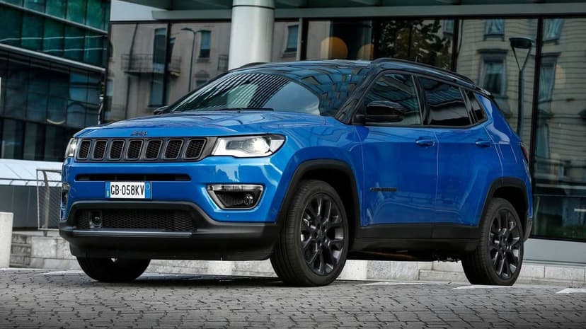 Blue Jeep Compass SUV with black wheels parked in front of a modern glass building in a city environment.