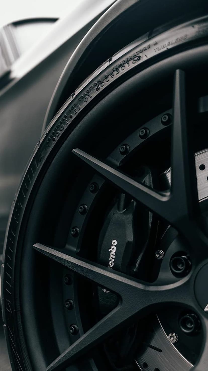 Black matte multi-spoke sports car wheel with a red Brembo brake caliper and detailed tire sidewall markings.