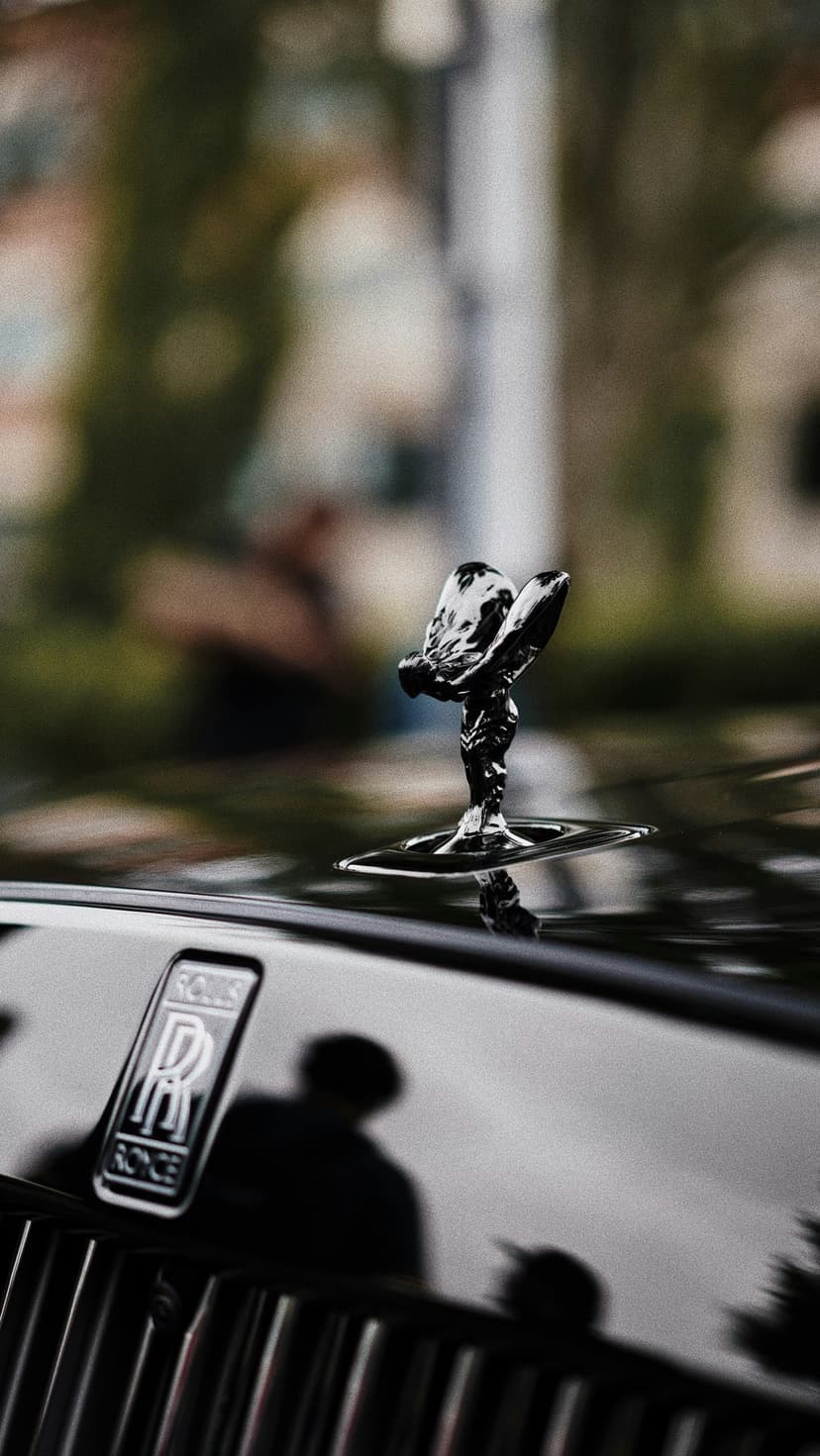 Spirit of Ecstasy figurine in black chrome atop a dark car hood with the RR logo visible in the foreground.