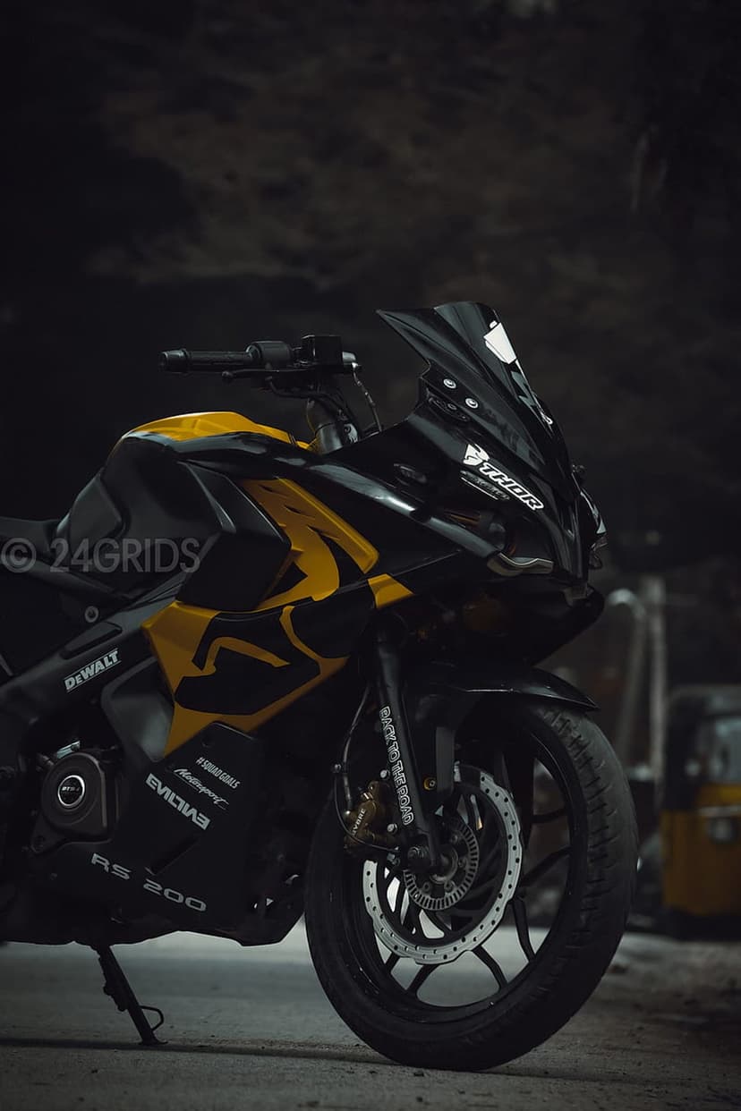 Black and yellow Pulsar RS 200 sportbike with a racing windshield and front wheel against a dark background.