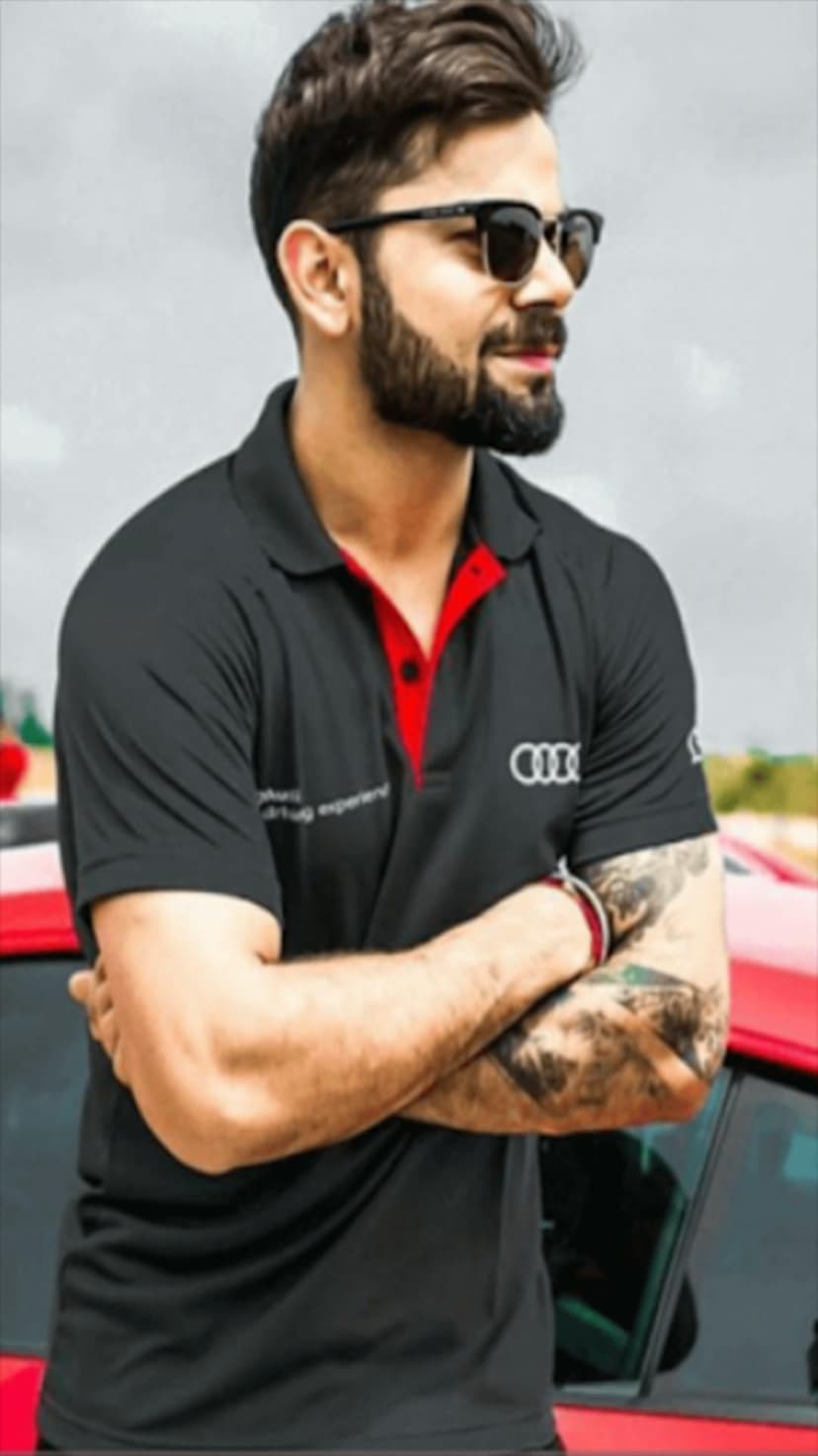 Virat Kohli wearing a black Audi polo and sunglasses while leaning against a red car with visible arm tattoos.