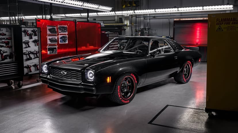 Black Chevrolet Camaro restomod with glowing LED headlights and red-lettered tires in an industrial garage.