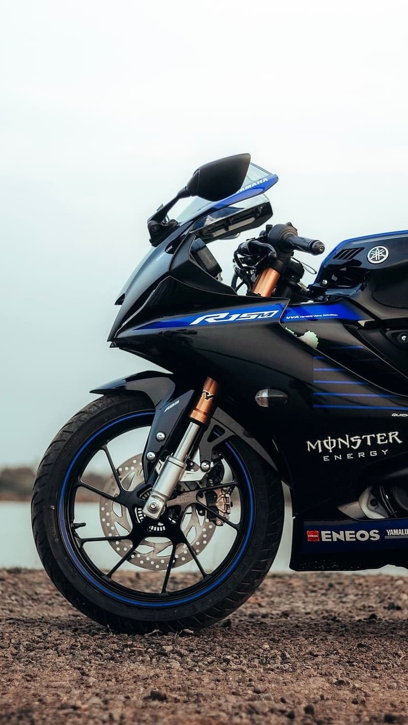 Yamaha R15 sportbike with Monster Energy livery parked on gravel near water with blue accents on the fairing.