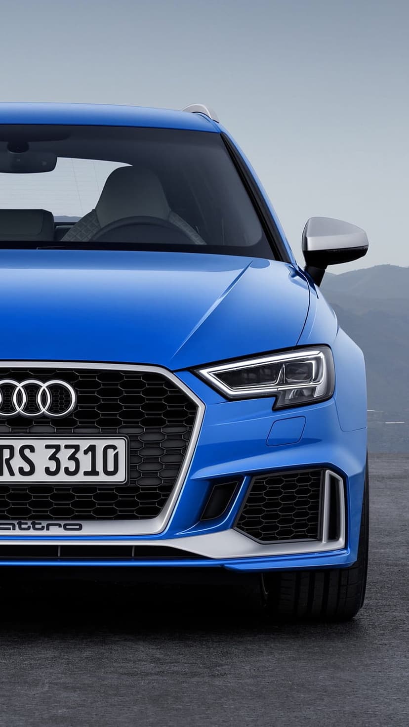 Blue Audi RS 3310 Quattro sports car front grille and LED headlights on a mountain road with a blurred background.