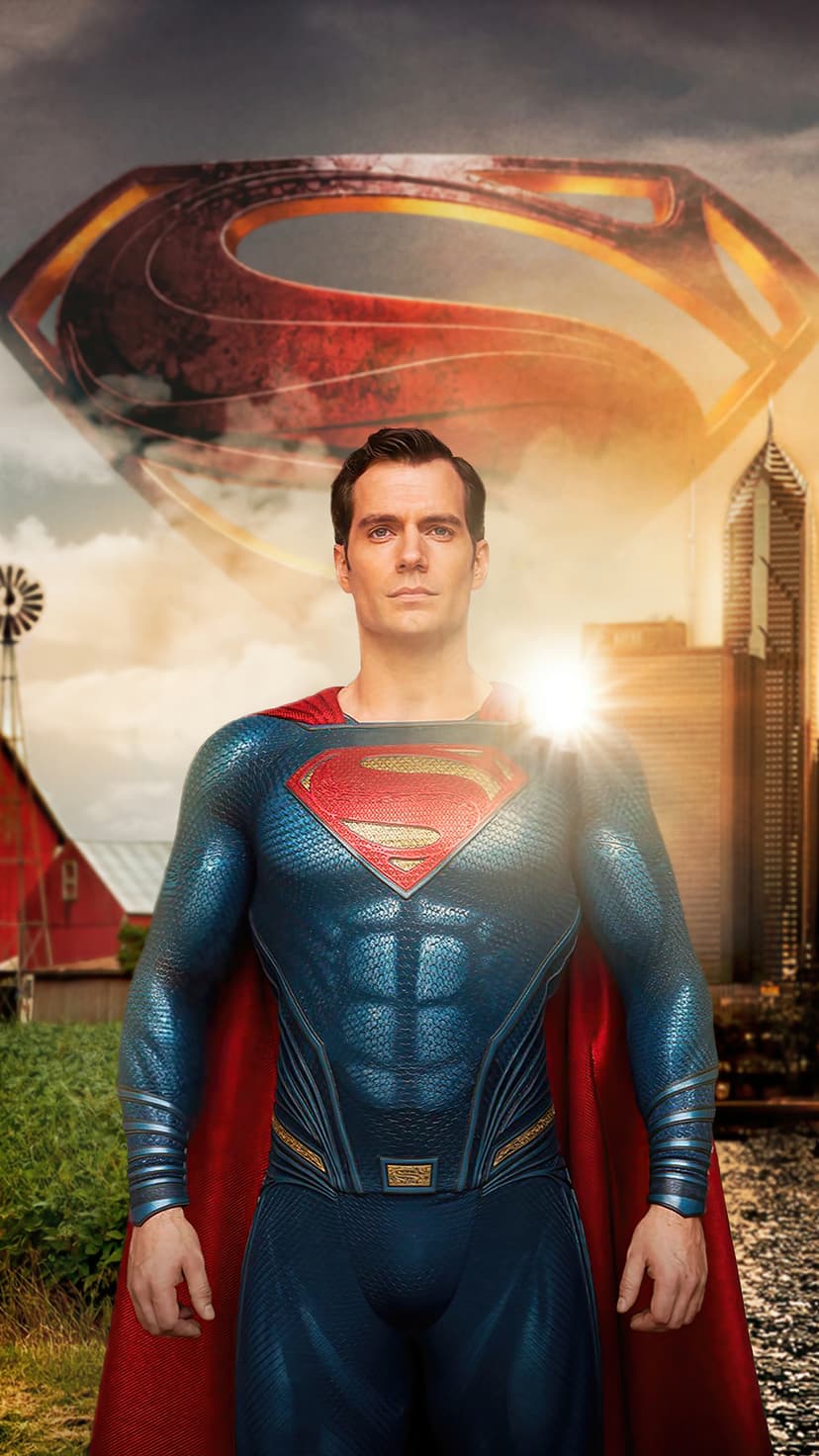 Superman in a textured blue suit with a red cape stands before a sunlit farm and a distant cityscape.