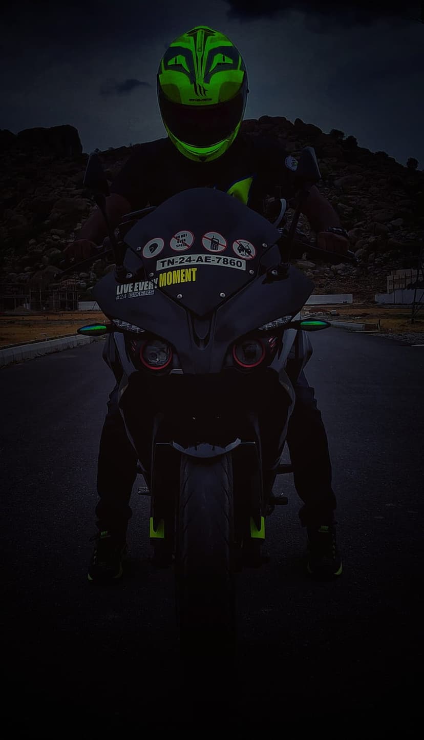 Motorcyclist in a neon green helmet sits on a black bike with red circular headlights against a rocky backdrop.