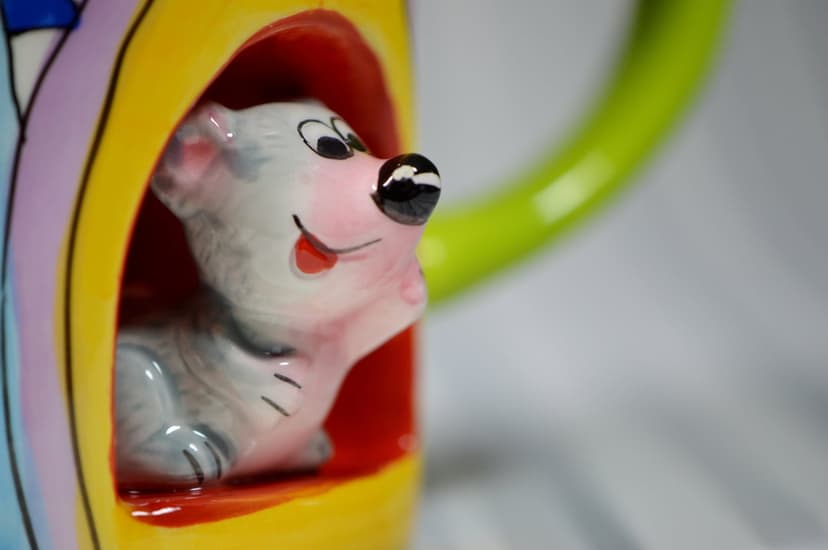 Smiling white dog figurine peeking out of a rainbow-patterned yellow ceramic cup with a bright green handle.