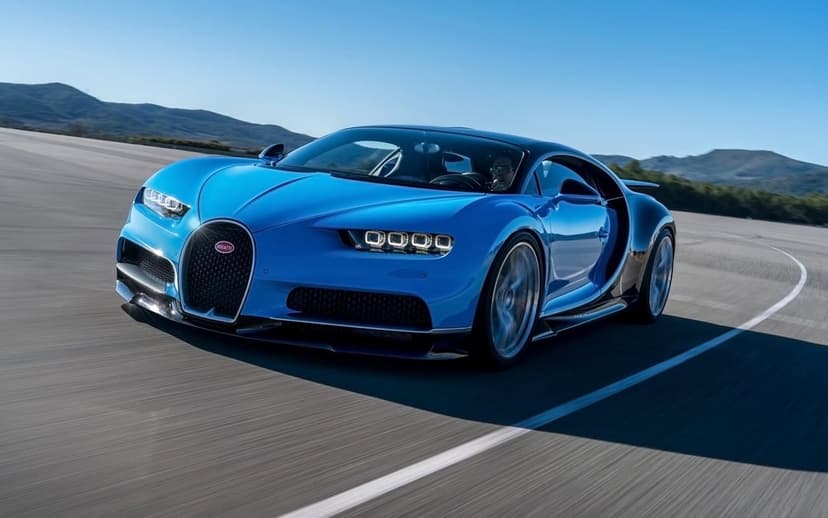 Blue Bugatti Chiron hypercar driving fast on a curved asphalt track with motion blur and clear blue sky background.