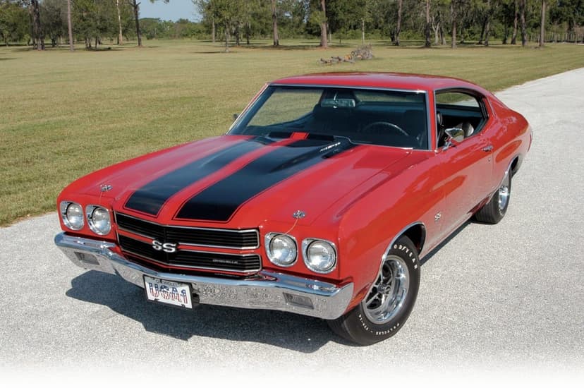 Red 1970 Chevrolet Chevelle SS with black racing stripes parked on a paved road in a green field.