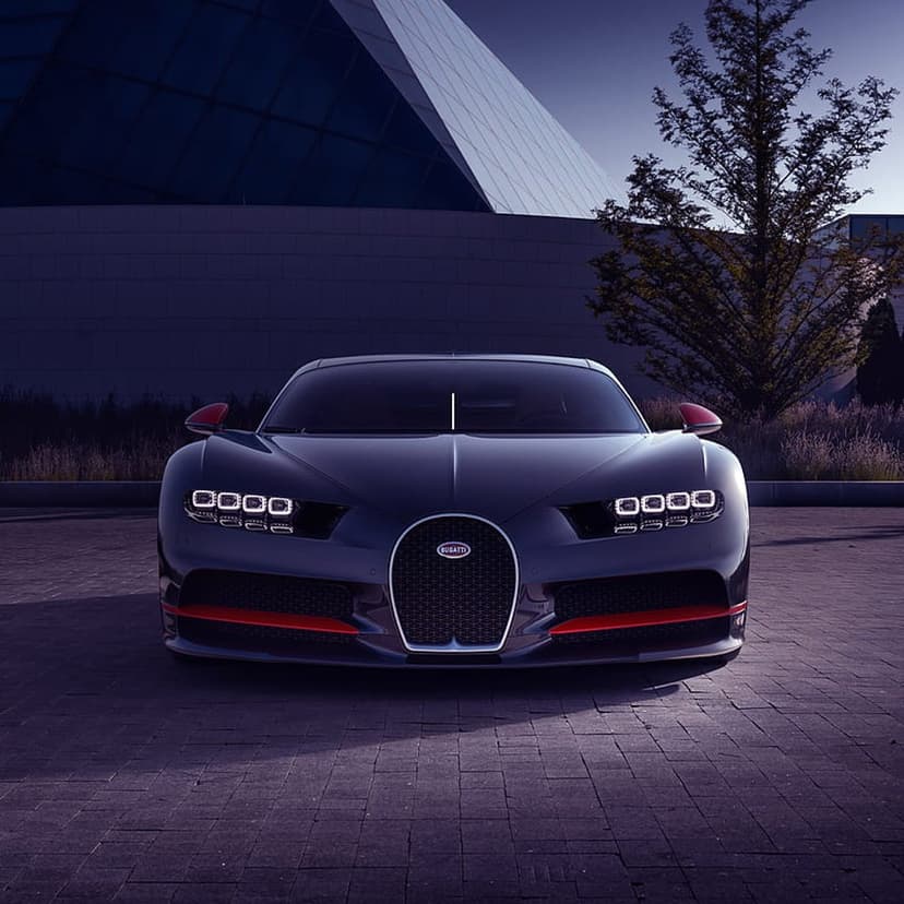 Dark blue Bugatti Chiron parked before a modern building and lone tree during a calm, dim twilight evening.