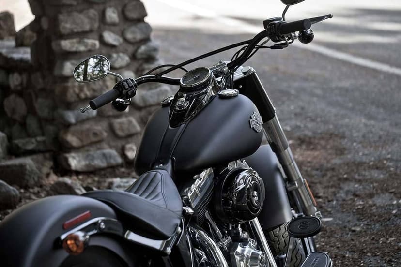 Close-up of a matte black motorcycle with chrome engine parts parked near a rustic stone wall on a road.