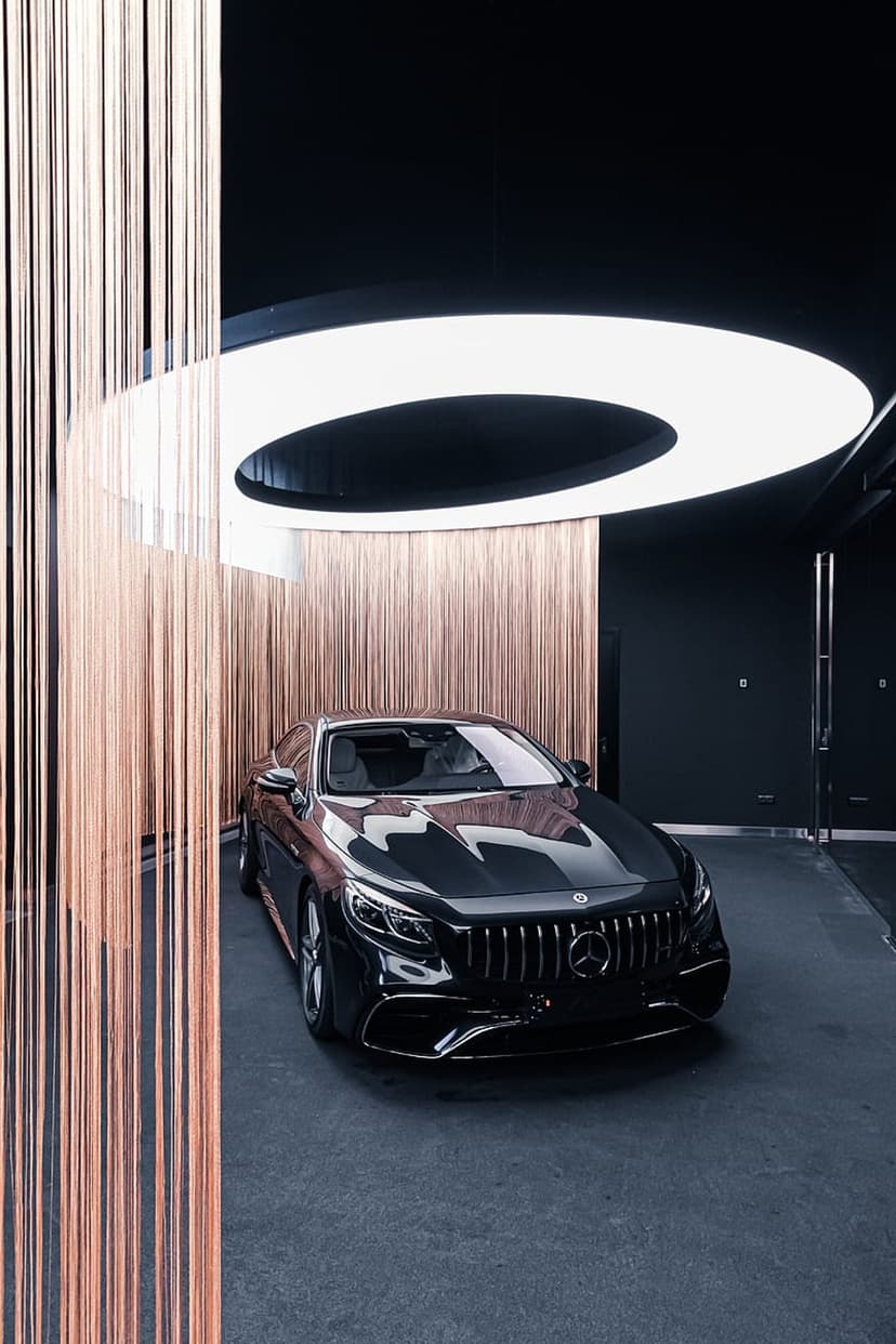 Black Mercedes S-Class Coupe parked in a dark showroom with copper vertical bars and circular ceiling illumination.