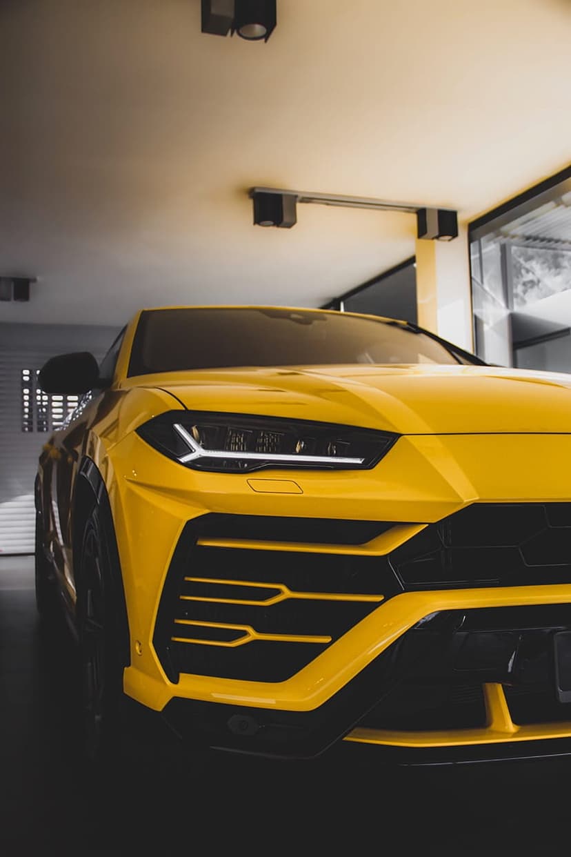 Yellow Lamborghini Urus SUV with glowing LED headlights and black grille in a sleek modern garage setting.