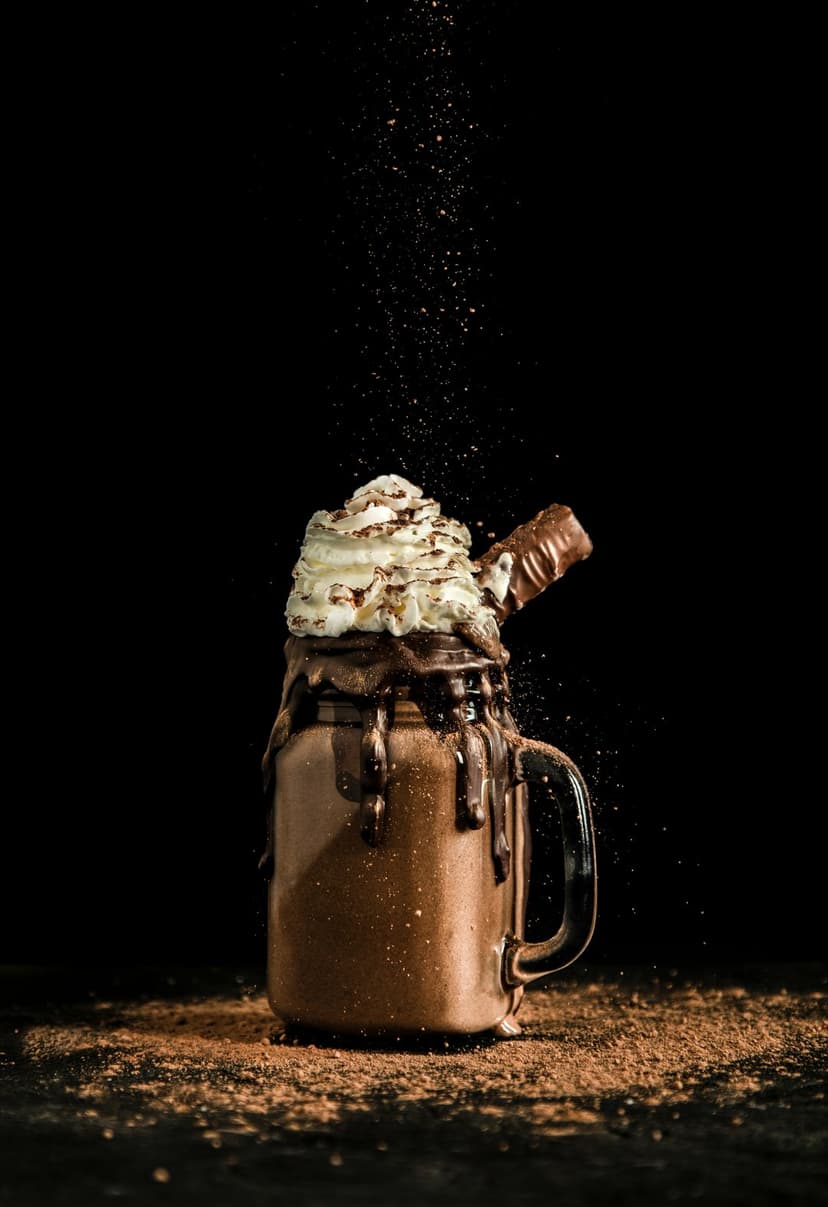 Chocolate milkshake in a glass jar topped with thick whipped cream and a candy bar against a dark background.