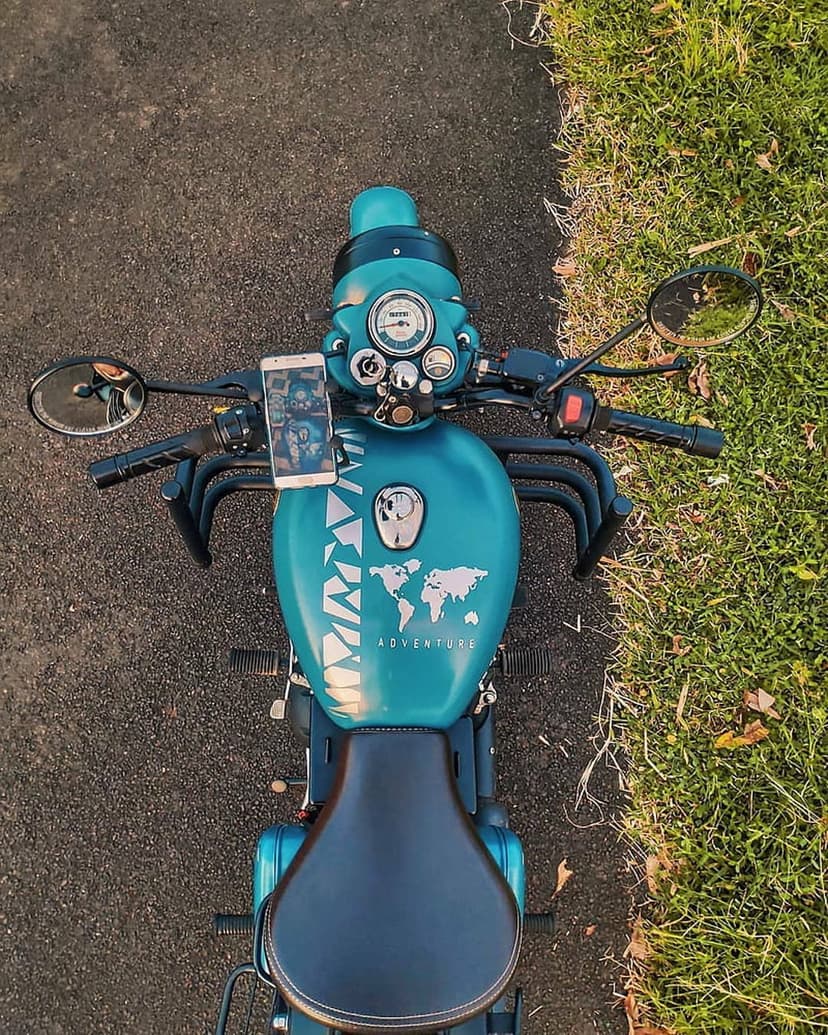 Turquoise motorcycle fuel tank with a world map decal and Adventure text seen from a top-down view.