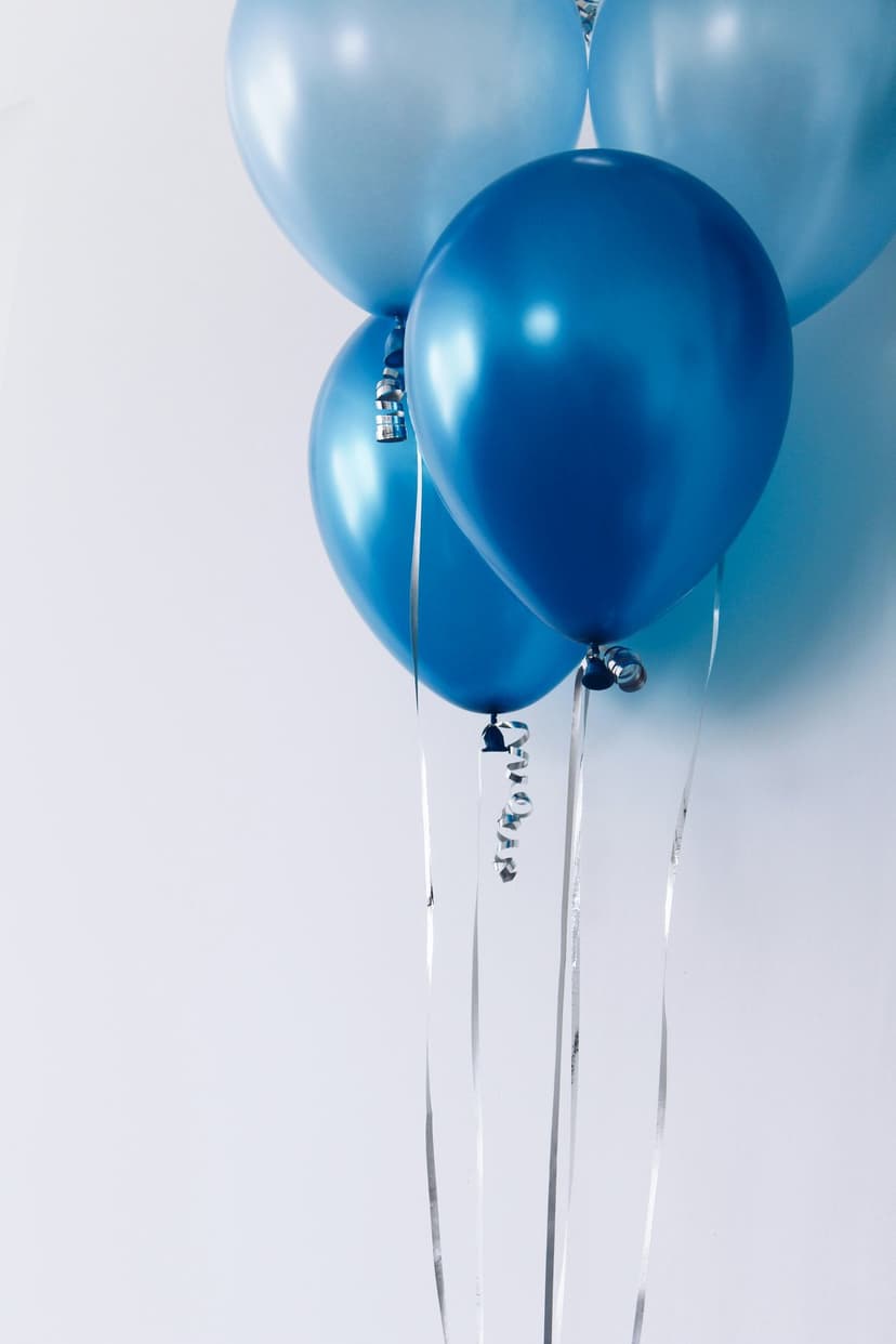 Blue balloons in varying shades float with curled silver ribbons against a plain white studio background.