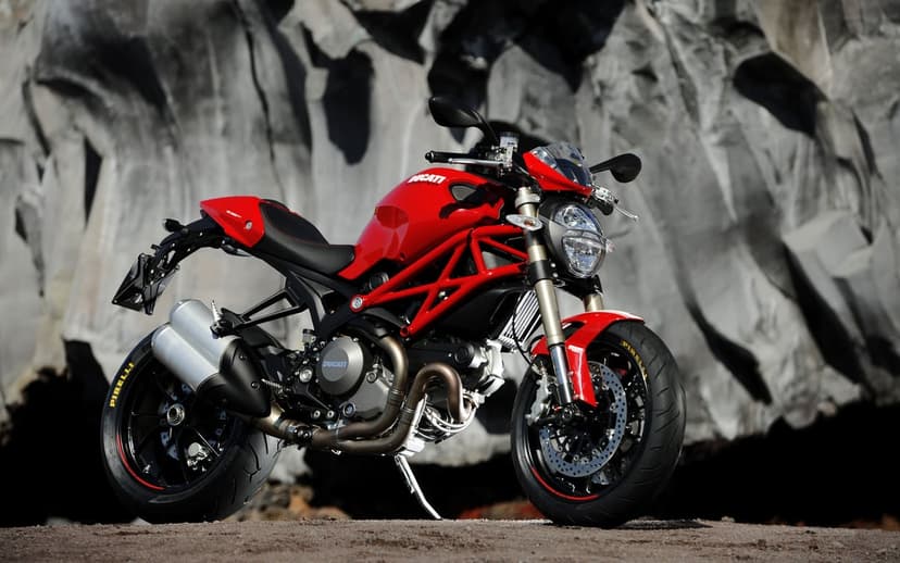 Red Ducati Monster 1100 motorcycle parked in front of a jagged gray volcanic rock formation under bright light.