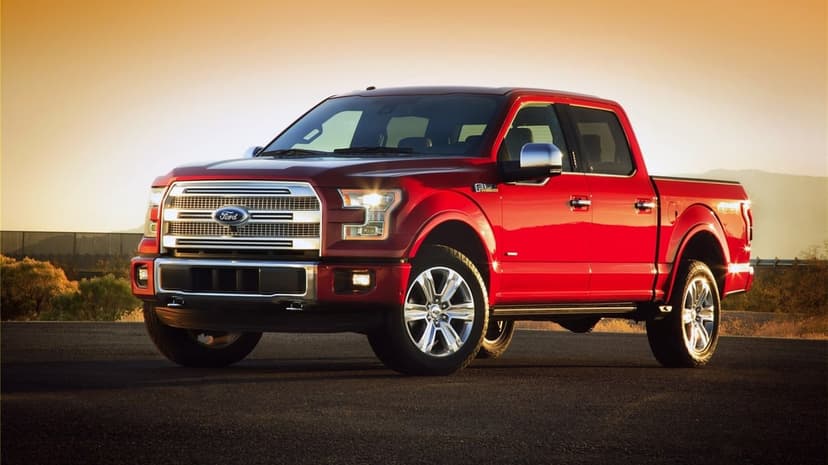 Red Ford F-150 pickup truck parked on a desert road under a warm golden sunset sky with chrome grille accents.