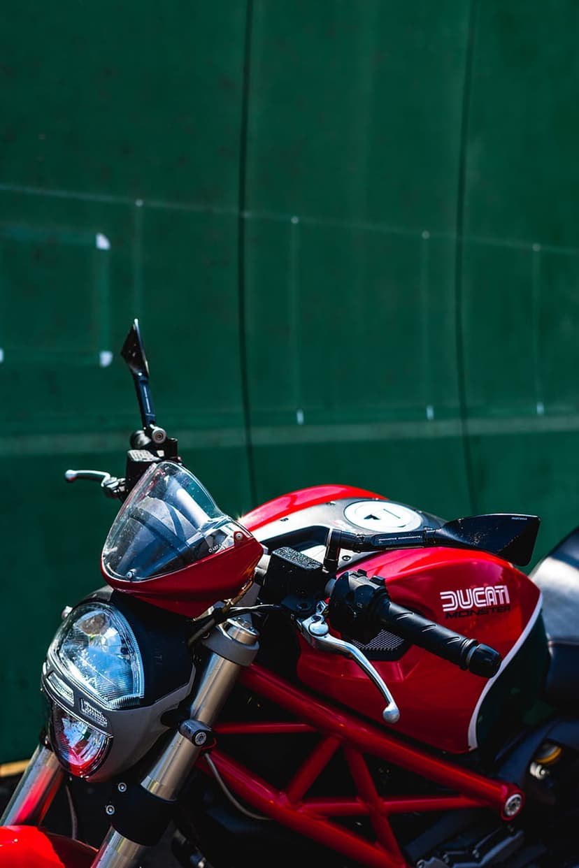 Red Ducati motorcycle headlight and handlebars with the brand logo against a textured dark green background.