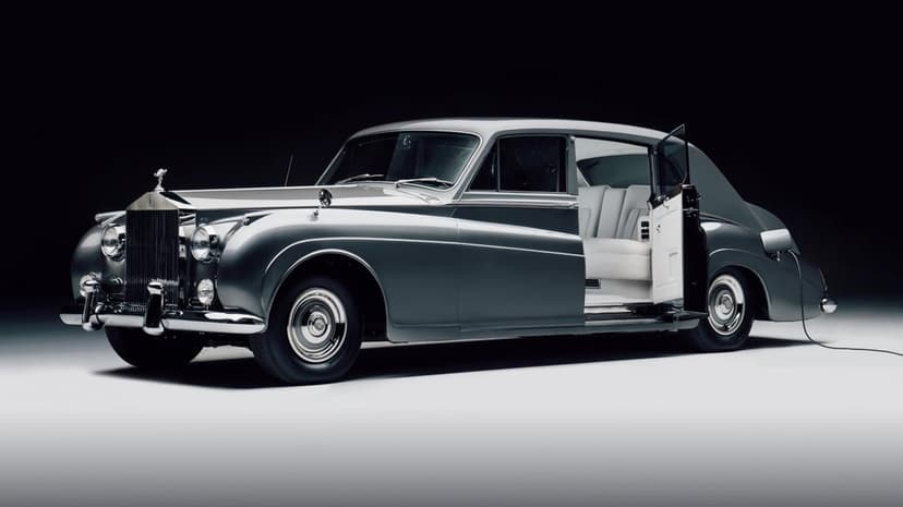 Silver vintage Rolls-Royce with an open rear door and white leather interior in a dark professional studio.