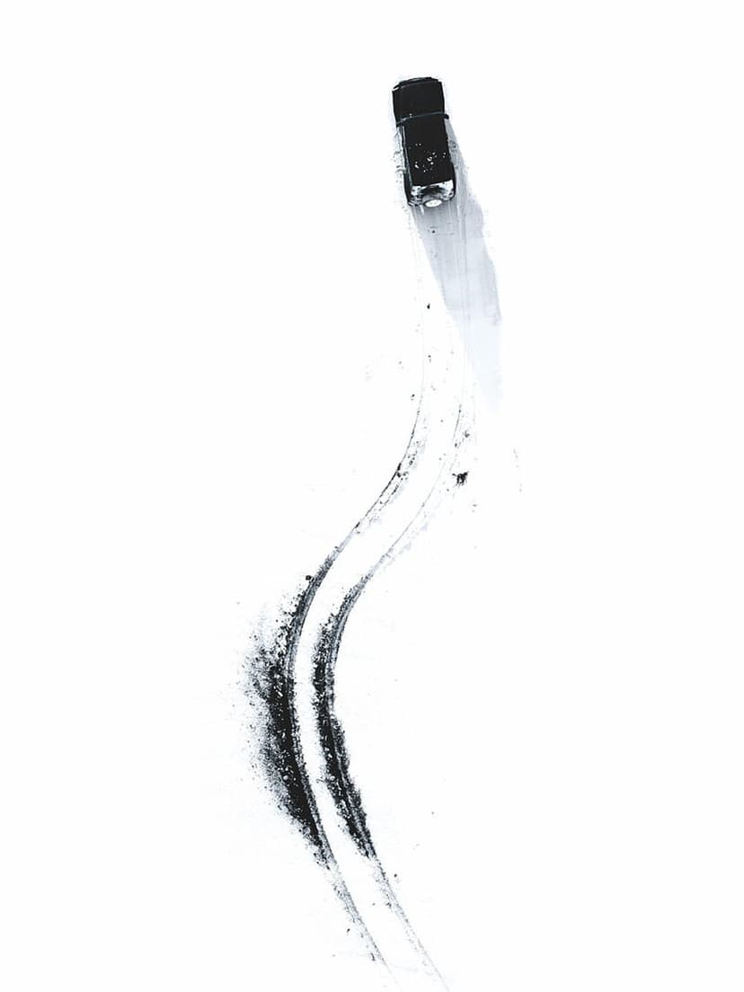 Black sports car drifting on a white surface leaving dark skid marks and smoke trails in a top-down view.