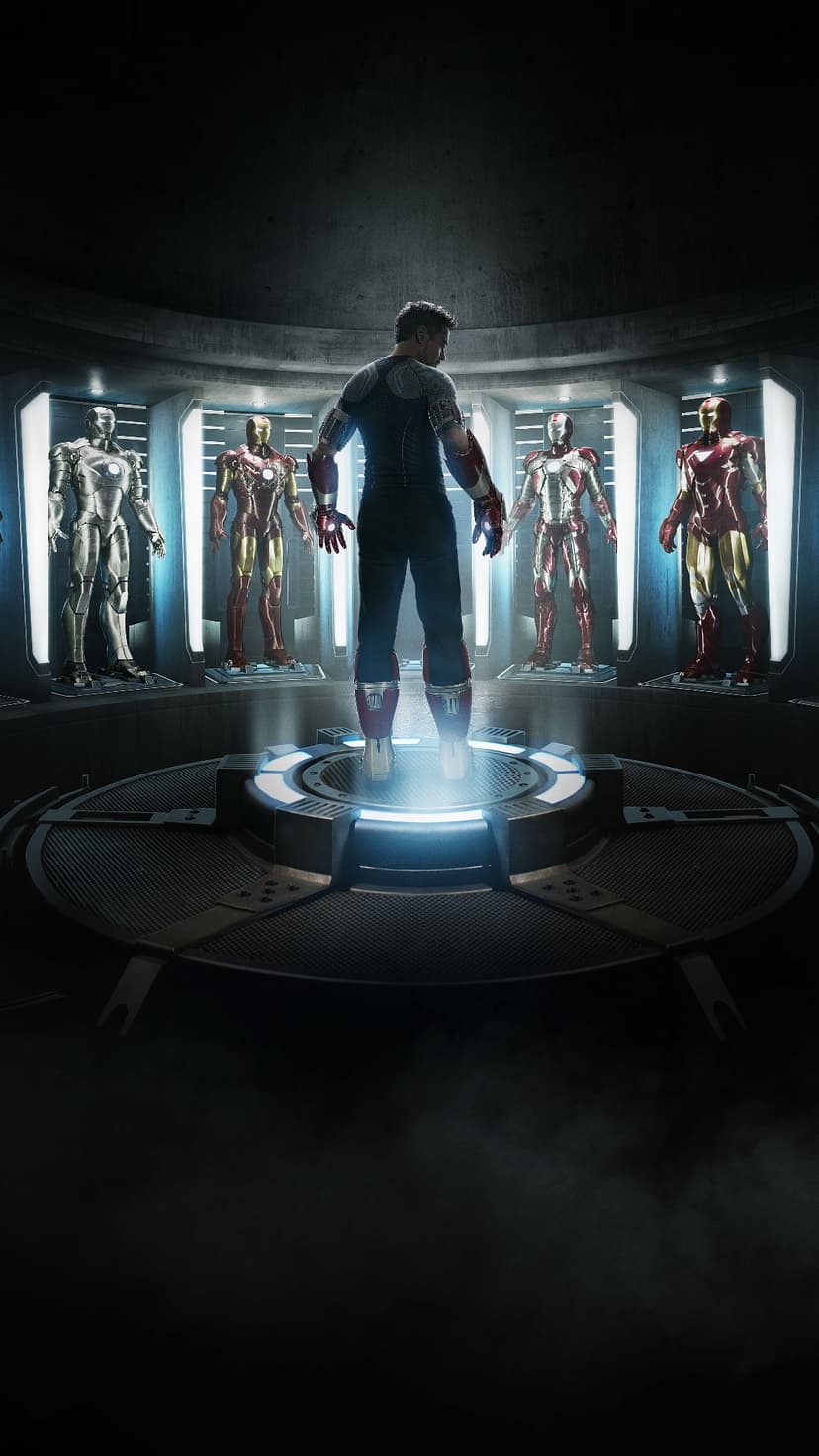 Tony Stark stands on a glowing circular floor plate surrounded by numerous Iron Man suits in glass display cases.